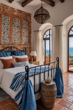 a bedroom with an iron bed, blue and white bedspread, two large windows and a view of the ocean