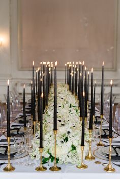 a long table with many black candles and white flowers on the centerpiece is set for a formal dinner