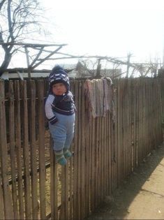 a young boy standing on top of a wooden fence