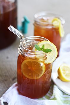 two mason jars filled with iced tea and lemon slices on a towel next to plates