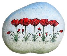 a painted rock with red flowers in the grass next to a blue sky and white background