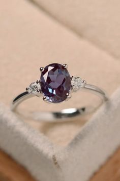 a ring with an oval shaped purple stone and three small white diamonds sits in a box