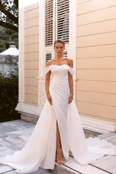 a woman in a white wedding dress standing on a porch next to a house with shutters