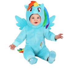 a baby in a blue unicorn costume sitting on the floor with his hands out and eyes closed