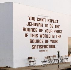 a large white building with a quote on it's side next to some tables and chairs