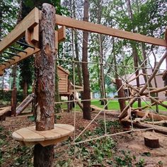 a wooden playground in the woods with swings and climbing ropes attached to it's posts