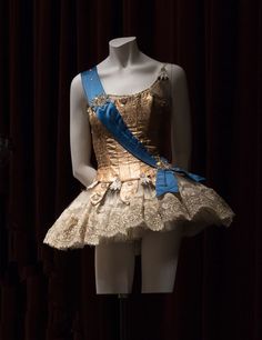 a mannequin wearing a gold dress with blue ribbon around the waist and shoulder