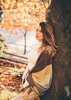 a woman leaning against a tree in the fall