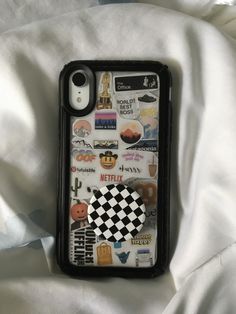 an iphone case with stickers on it sitting on a white cloth covered bed sheet