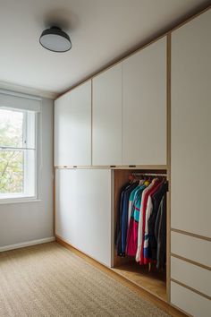 an empty room with white cabinets and clothes hanging on hangers in front of a window