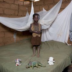 a young boy standing on top of a bed next to stuffed animals and mosquito nets