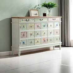 a white dresser with flowers painted on it in a room next to a potted plant