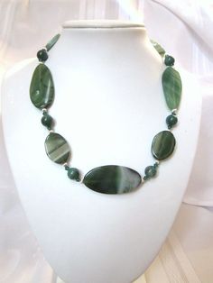 "Beautiful Green and White Striped Agate Beads in graduated ovals and rounds are combined with Swarovski Crystals in this lovely creation.  Swarovski crystal emerald green bicones accent the agates nicely.  This necklace will go with any outfit from casual to elegant.  This necklace is 18\" long with an additional 2.5\" chain extender, finished with a lobster claw clasp.  The necklace was created using: 10 mm striped round agates, 25x50mm elongated oval agates, 23x30mm flat oval agates, Swarovski emerald green 4mm bicone crystals, and 4mm fluted spacer rounds.   Agate is a variety of chalcedony with multi-colored curved or angular banding.  This is a variety of quartz. The colors are arraigned in stripes or bands.  According to Gemstone Folk lore: Agate is believed to discern truth, accept Elegant Green Oval Beads Jewelry, Green Oval Polished Beads Jewelry, Elegant Green Oval Bead Necklaces, Elegant Green Necklaces With Oval Beads, Elegant Green Oval Beaded Necklaces, Elegant Oval Agate Beads And Cabochons, Elegant Agate Oval Beads, Green Oval Jade Beads Jewelry, Elegant Oval Agate Beads