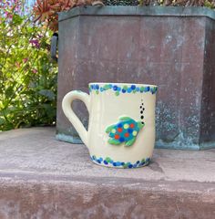 a ceramic coffee cup sitting on top of a stone slab in front of some potted plants