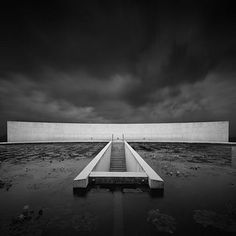 a black and white photo of a concrete structure in the middle of water with dark clouds overhead