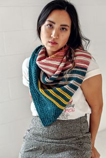 a woman standing in front of a white wall wearing a striped scarf and plaid skirt