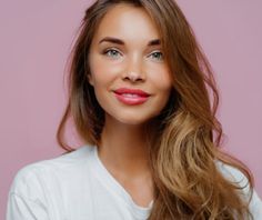 a beautiful young woman with long brown hair posing for a photo in front of a pink background