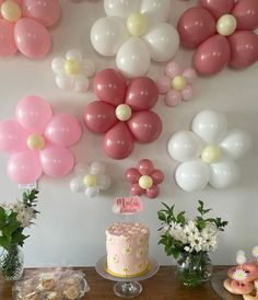 a table topped with a pink cake and lots of balloons above the desserts on top of it