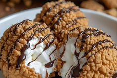 three cookies covered in ice cream and drizzled with chocolate on a plate