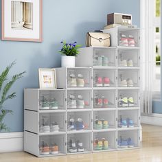 there are many pairs of shoes in the storage bins on the floor next to a plant