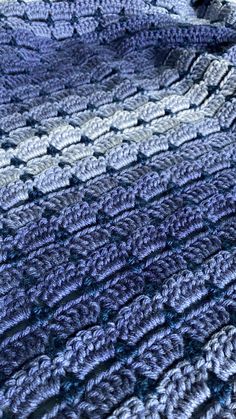 a crocheted blanket is laying on top of a bed with blue and gray colors