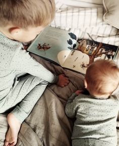 two young children laying in bed reading a book to each other, with the child looking at it