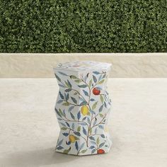 a ceramic vase sitting on top of a white table next to a bush covered in green leaves