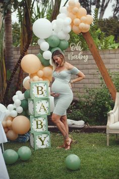 a pregnant woman standing in front of a baby sign with balloons on the grass and greenery