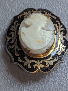 "Antique Shell Cameo & Black Enamel Brooch Pin HALLMARKS Unmarked. MEASUREMENTS 1 3/8\" x 1 5/8\".               MATERIALS Shell, Black Enamel, Gold Gilt. CONDITION In very good condition with minimal wear on gold gilt, please use all pictures as part of item's description. Turn of the Century Edwardian era Mourning Cameo brooch featuring carved shell center of classic Roman or Grecian lady in profile prong set in Black Enamel frame with ornate Gold Gilt designs. This is a very unique cameo. Cam Ornate Medallion Brooch For Formal Occasions, Victorian Brooches For Ceremonial Occasions, Ornate Oval Brooch For Formal Occasions, Ornate Medallion Brooches For Formal Occasions, Ornate Oval Brooches For Formal Occasions, Victorian Brooches With Intricate Design, Victorian Engraved Medallion Brooches, Formal Engraved Brooches, Antique Filigree Brooch For Formal Occasions