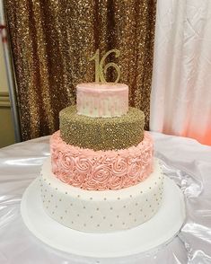 three tiered cake with pink and gold frosting on top sitting on a table