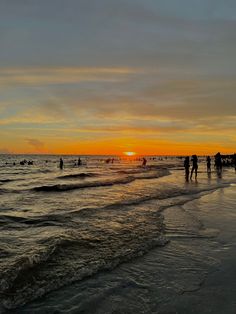 people are standing on the beach at sunset