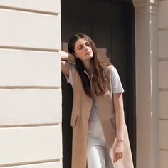 a woman leaning against a wall with her hand on her head and looking off to the side