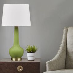 a green vase sitting on top of a wooden table next to a lamp and chair