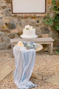 a wedding cake sitting on top of a table next to a stone wall and bench