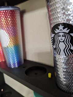 two starbucks cups sitting on top of a shelf