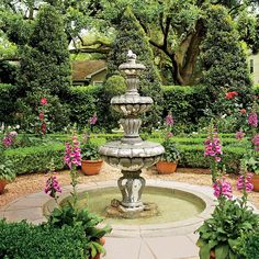 a fountain surrounded by potted plants and flowers in the middle of a garden area