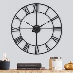 a large clock on the wall above a shelf with some books and a glass vase