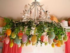 a chandelier hanging from the ceiling with eggs painted on it and plants in front