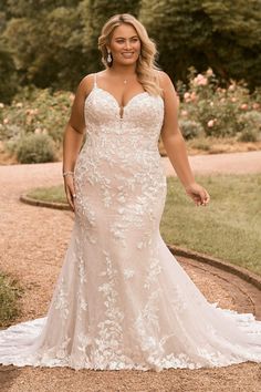 a woman in a wedding dress standing on a path with trees and bushes behind her