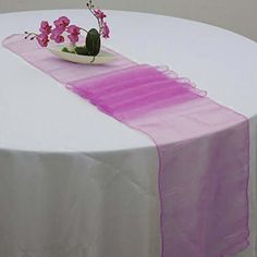 a white table topped with a vase filled with pink flowers next to a purple ribbon