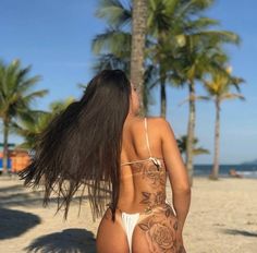 a woman sitting on the beach with her back to the camera and tattoos on her body