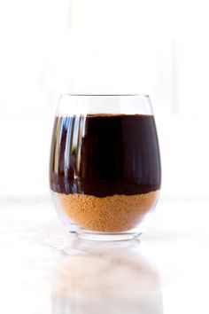 a glass filled with brown liquid sitting on top of a white counter next to a window