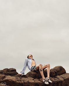 a man sitting on top of rocks with his feet up in the air while wearing swimming trunks