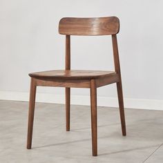 a wooden chair sitting on top of a cement floor next to a white wall in an empty room