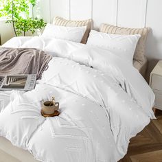 a bed with white comforter and pillows on top of it next to a potted plant