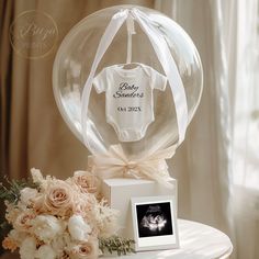 a baby announcement in a clear glass ball on top of a table next to flowers