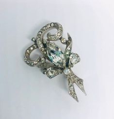 Exquisite vintage rhinestone bow brooch. Rhodium plated metal in a ornate scrolling design and pave set rhinestones brooch. Large center rhinestone. Wonderfully detailed.... including rhinestone set upturned leaves. Absolutely gorgeous!! In excellent vintage condition with minimal age appropriate wear. All stones securely prong and pave set. Roll over clasp secure. Measures 1 5/8 inches tall by just over 1 inch wide. Beautiful!! Antique Jeweled Brooch For Wedding, Silver Jeweled Brooches For Formal Occasions, Formal Silver Jeweled Brooches, Victorian Jeweled Wedding Brooches, Antique Rhinestones Brooch For Vintage Events, Elegant Silver Brooch With Screw Back, Antique Rhinestone Brooches For Vintage Events, Vintage Diamond Accented Brooches For Evening, Vintage Silver Brooches With Diamond Accents