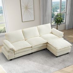 a living room with a large white sectional couch and rugs on the floor in front of windows