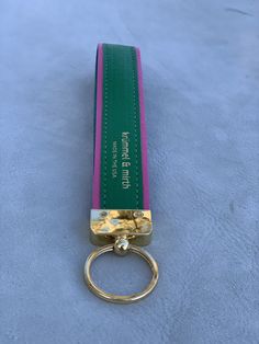 a green and pink keychain sitting on top of a blue surface with a gold ring