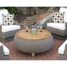 an outdoor seating area with wicker furniture and pillows on the brick floor next to a stone wall